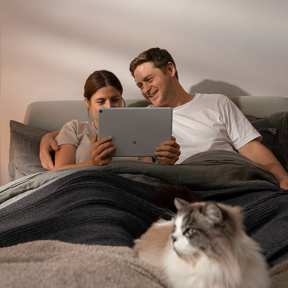 Kvinne og mann i sengen ser på Google TV på Google Pixel Tablet og en katt