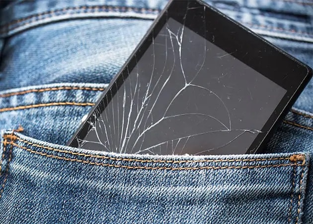 smarttelefon med knust skjerm i en jeans-lomme
