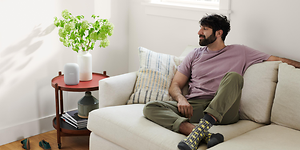 Man sittin in a white sofa while listening to something on his Google Nest Audio