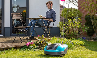 mann sitter på stol og leser i hagen med robotgressklipper på gressplen