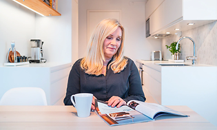 kvinne leser magasin ved kjøkkenbord på hvitt kjøkken fra epoq
