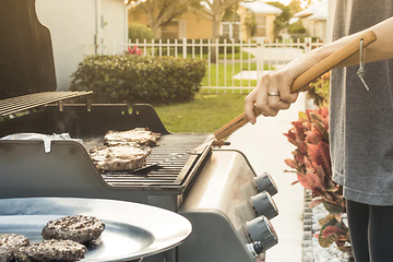 person griller hamburger ute i hagen på gassgrill