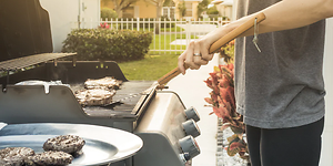 person griller hamburger ute i hagen på gassgrill