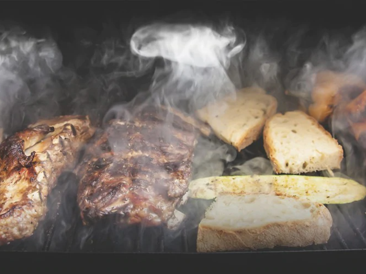 kjøtt og grønnsaker røkes på grillrist i en grill