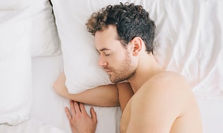 mann sover med arm under pute i en seng