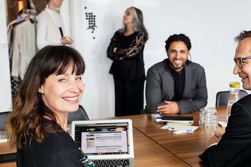 kvinne og to menn som sitter ved et konferansebord og smiler og jobber på en laptop