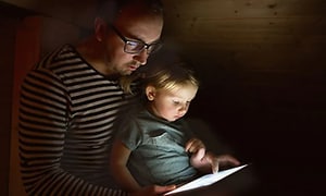far og datter bruker nettbrett sammen i et mørkt rom