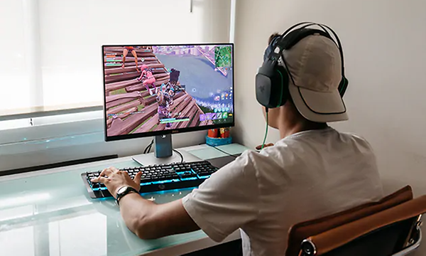 gutt med caps sitter foran gaming-pc med hodetelefoner på