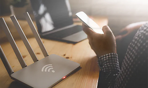 person holder smarttelefon ved siden av router foran laptop