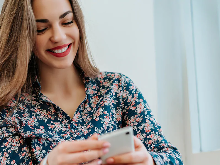 Kvinne smiler og ser på telefonen sin