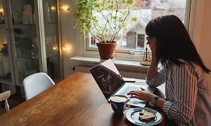 kvinne sitter ved et kjøkkenbord med en bærbar pc på hjemmekontor