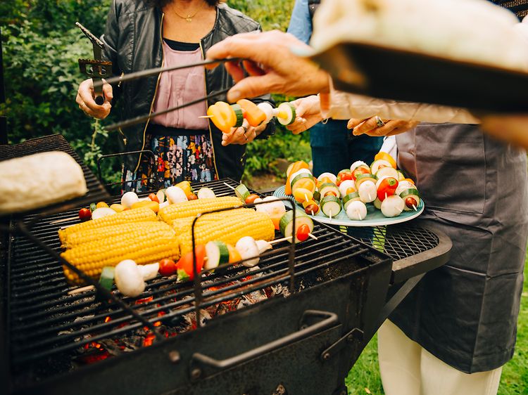 Mennesker som står rundt en kullgrill og lager mat