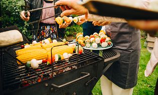 Mennesker som står rundt en kullgrill og lager mat