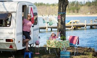 En campingvogn parkert ved vann, kvinne og barn utenfor