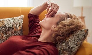 Kvinne med sinussmerter og hodepine som ligger på sofa