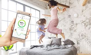 Mor som hopper på en seng med datter, mens du ser Airhtings-appen på smarttelefon foran