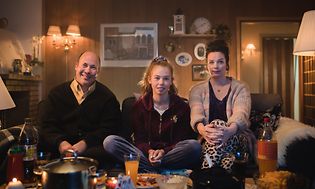 Familie på tre som sitter på en sofa