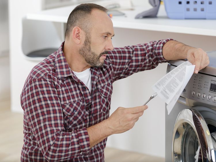 En mann sjekker instruksjonene når han installerer en vaskemaskin