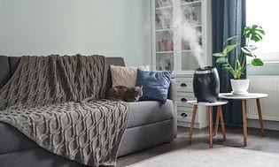 Svart luftfukter i en stue på et hvitt bord ved siden av en grå sofa