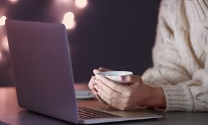 Person working with a laptop in the evening and holding a cup of coffee in their hands