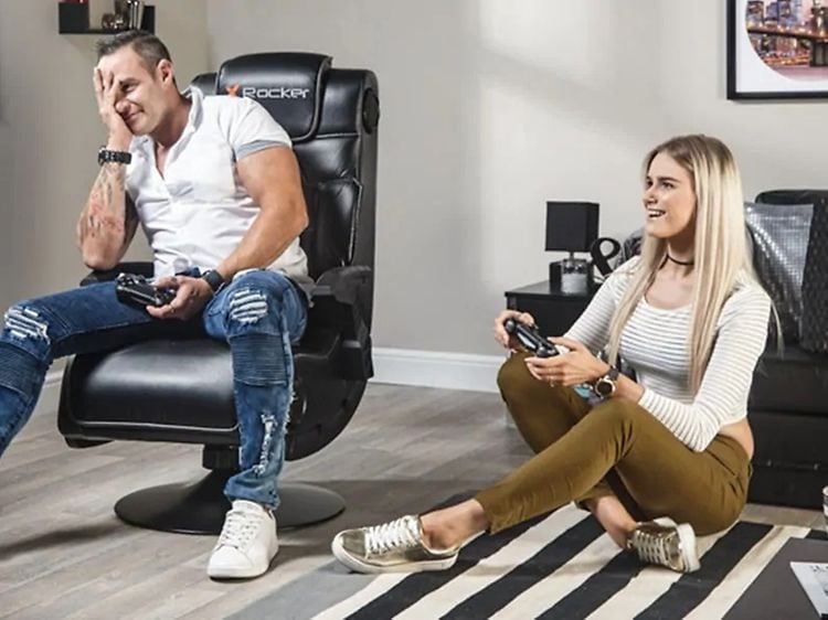 Mann sitter i en X Rocker gaming-stol og kvinne sitter på gulvet mens de spiller et konsoll-spill