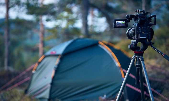 Kamera på stativ peker mot et telt i skogen i bakgrunnen