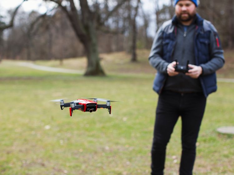 Mann som flyr drone utendørs mellom noen trær