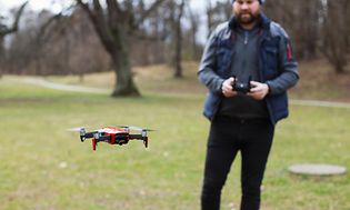 Mann som flyr drone utendørs mellom noen trær