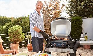 smilende mann bruker elektrisk grill mens han ser på en smilende kvinne som sitter ved et bord