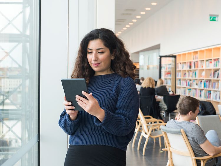 Kvinne som står i bibliotek med nettbrett