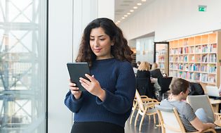 Kvinne som står i bibliotek med nettbrett