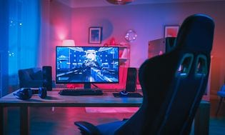 Gaming-oppsett i et rom. Skjerm, tastatur og høyttalere på et PC-bord med gamingstol sett i front
