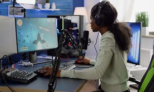 Jente som sitter foran sin stasjonære gaming-PC og strømmer