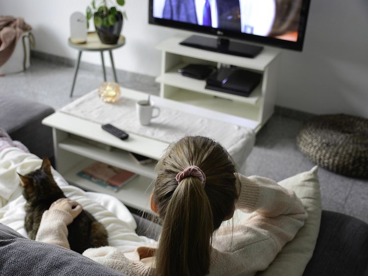 Kvinne som sitter på sofa med katt og ser på TV