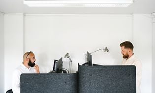 To menn i åpent kontorlandskap som jobber på PCene sine
