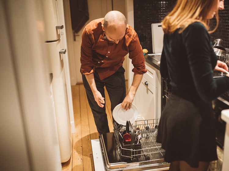 Mann og kvinne på kjøkken. Mannen putter oppvasken i oppvaskmaskinen mens kvinnen lager mat