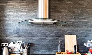 Ventilator over platetopp med forskjellige kjøkkenredskaper på kjøkkenbenken ved siden av