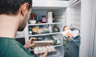 Mann som ser på en pakke egg i kjøleskapet