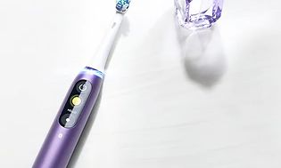 Oral-B iO serie 8 lilla elektrisk tannbørste liggende på et bord med en parfymeflaske