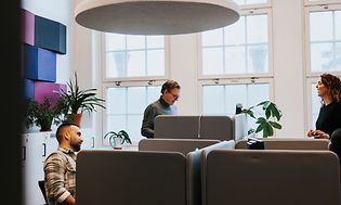 Tre personer i et åpent kontorlandskap