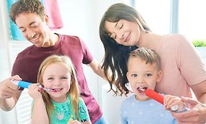 En mann og en kvinne hjelper en gutt og ei jente med å børste tennene med elektrisk tannbørste til barn fra Oral-B