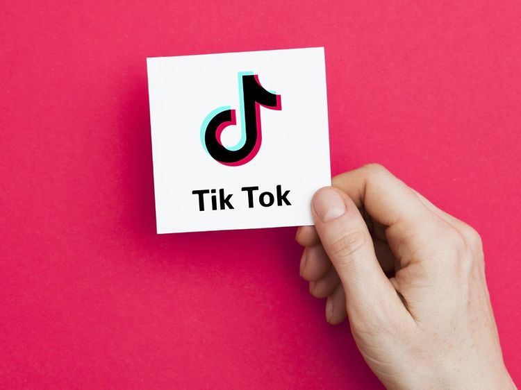 Hånd holder hvitt kort med TikTok-logo på en rosa bakgrunn