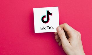 Hånd holder hvitt kort med TikTok-logo på en rosa bakgrunn