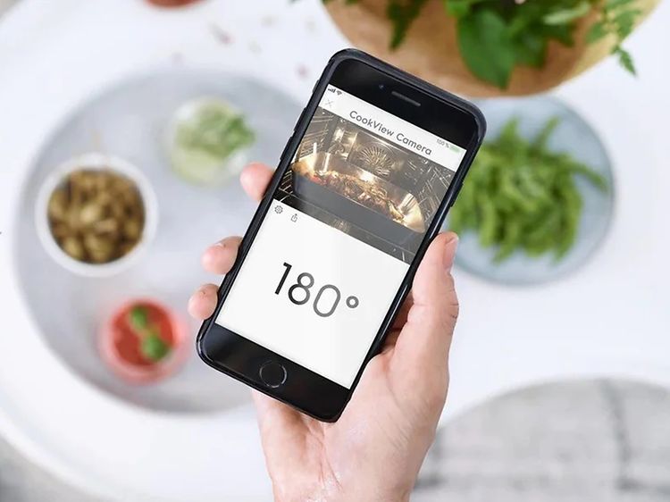 Hånd holder smarttelefon med app som viser smartovn og temperaturen på ovnen på skjermen