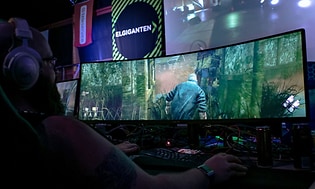 En gamer spiller et spill på en vid gaming-skjerm fra Elkjøp