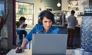 En kvinne sitter med hodetelefoner på og ser på sin Lenovo Legion på en kafé