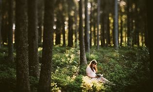 kvinne kledd i hvite klær leser en bok i skogen