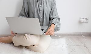 Kvinne sitter på gulvet og lader laptopen sin
