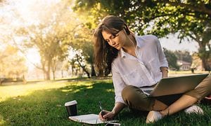 Kvinne som sitter i en park og jobber med laptopen sin