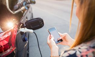 Kvinne som holder telefonen og lader bilen